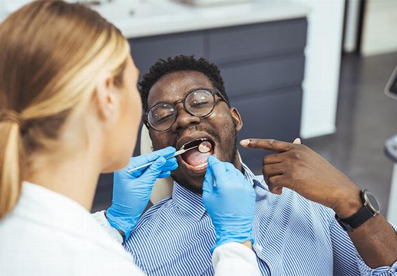 Man pointing at mouth while dentist looks at his teeth
